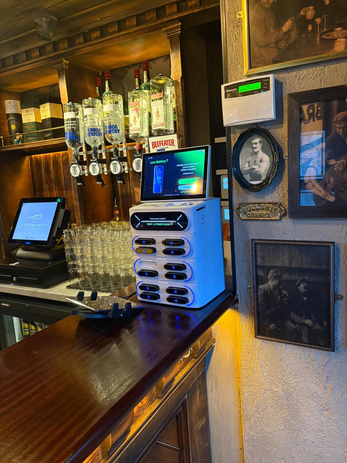 White power bank rental station on a bar counter with liquor bottles and vintage photos.